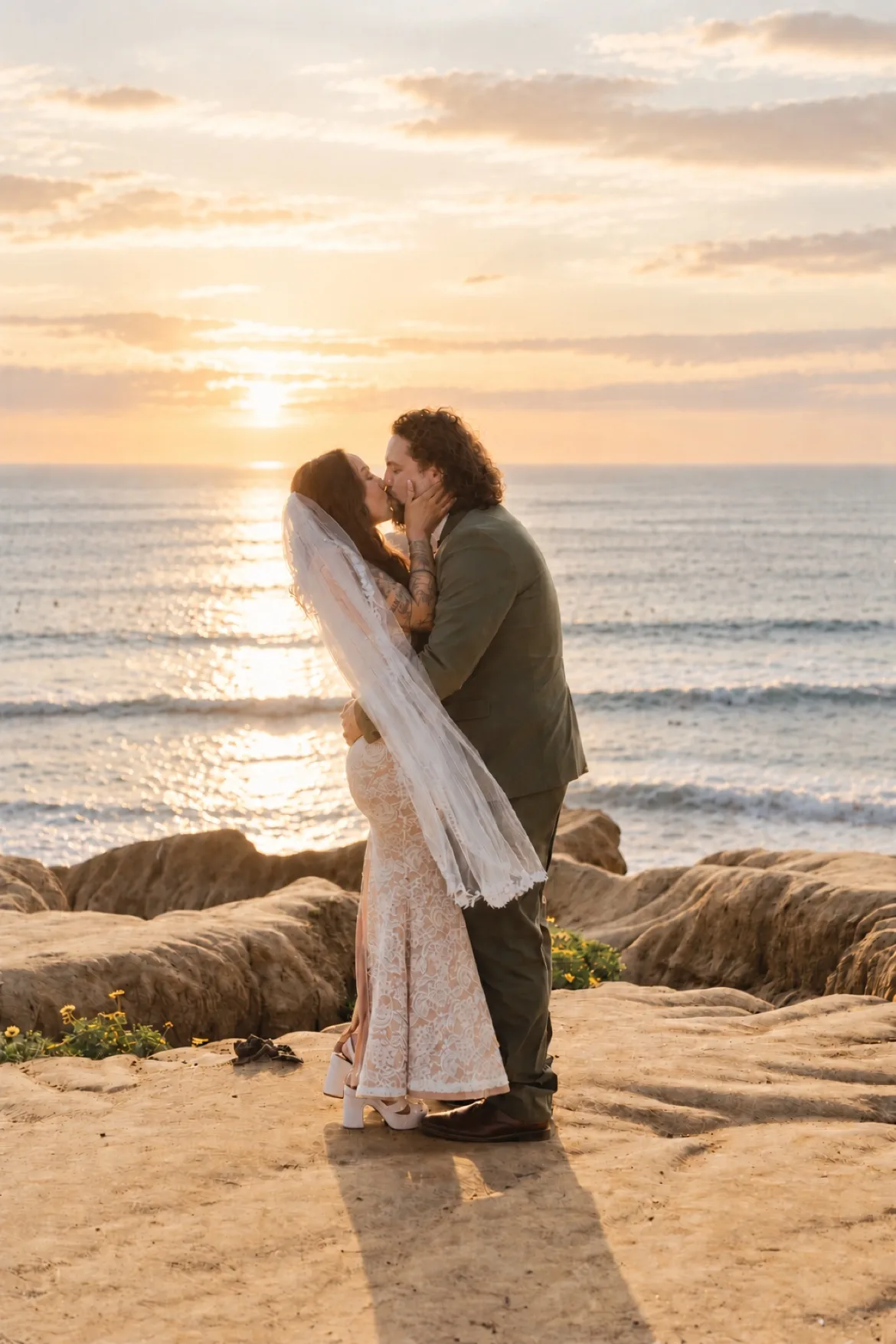 Couple kissing on the cliffs at sunset, her veil flowing